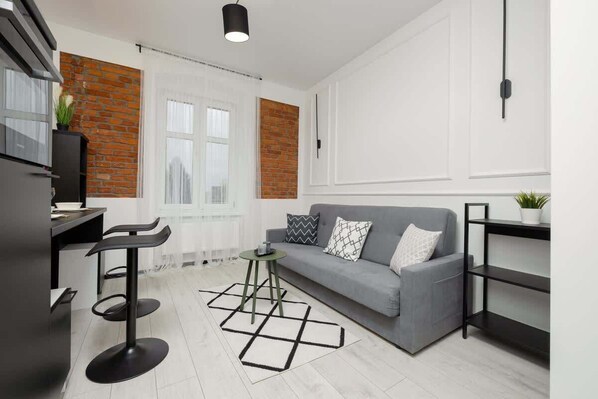 A modern kitchen with a grey sofa, black bar stools, and a geometric rug. - Stylish Studio in the center of Lodz | Smart TV | WiFi (Lódz)