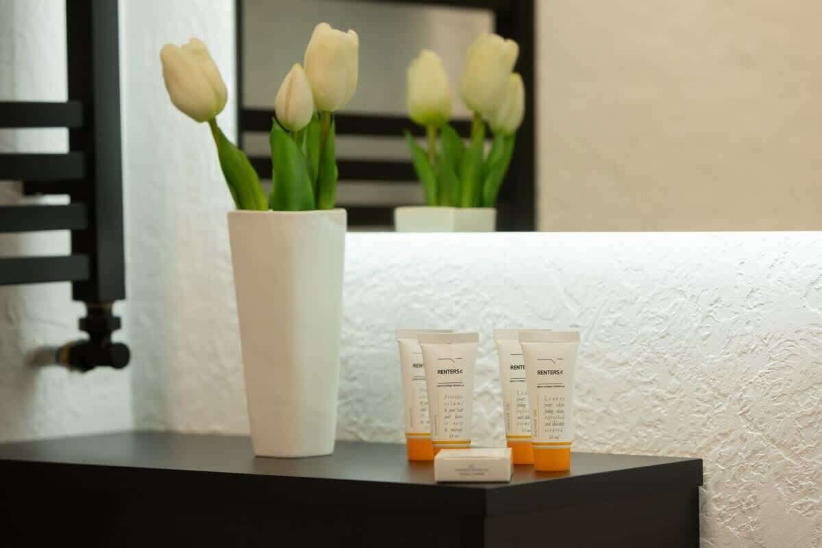 A white vase with white tulips and three RENTERS® skincare tubes on a black surface.