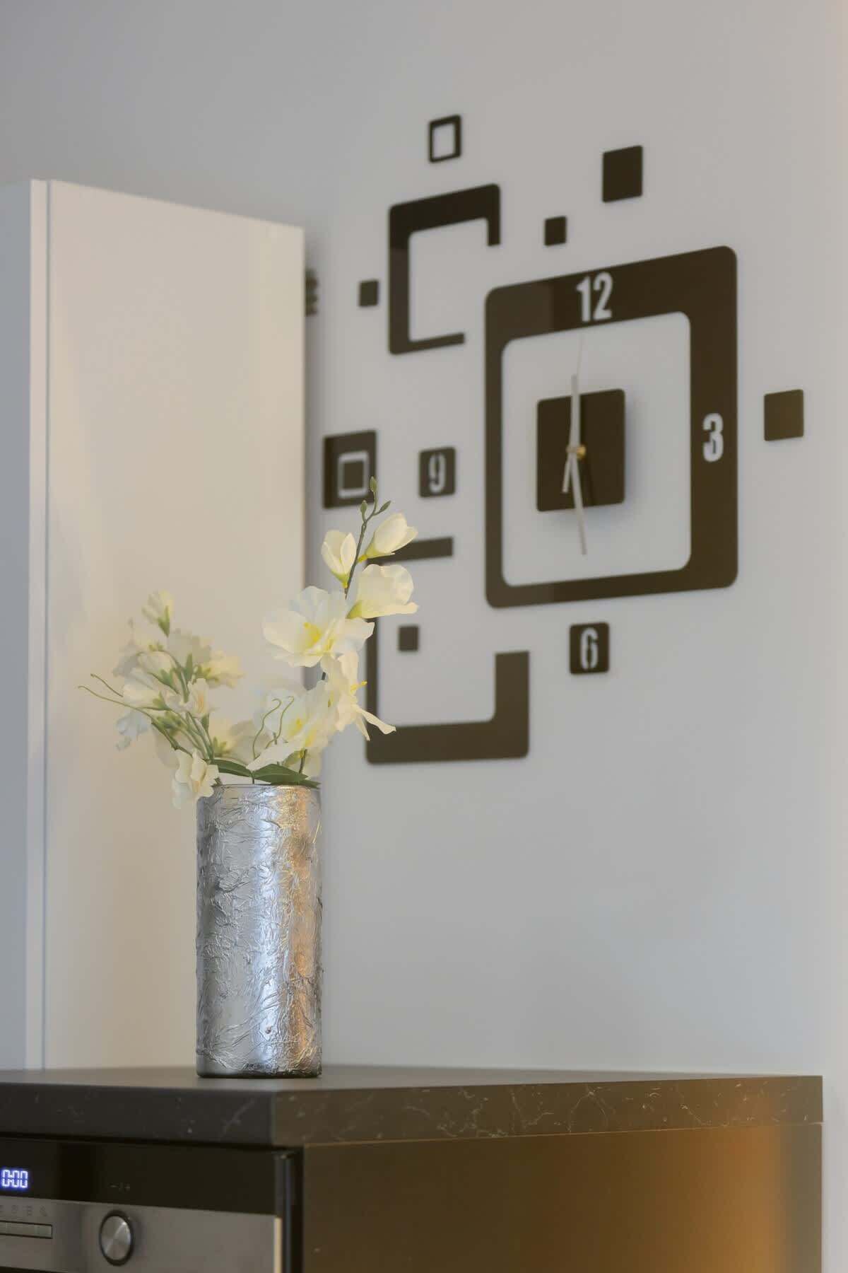 Um relógio de parede com design minimalista, um vaso decorativo com flores e um relógio digital em um armário.