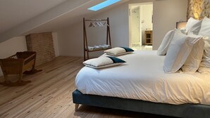 Una camera da letto con un lucernario, una panca di legno, un appendiabiti e vista su un bagno.
