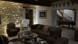 Un soggiorno rustico con parete in pietra, soffitto in legno, divano in pelle marrone, tavolino in vetro e tavolo da biliardo.