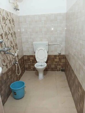 A bathroom with a toilet, a shower, and a blue bucket. - Chandan Resort (Puri)