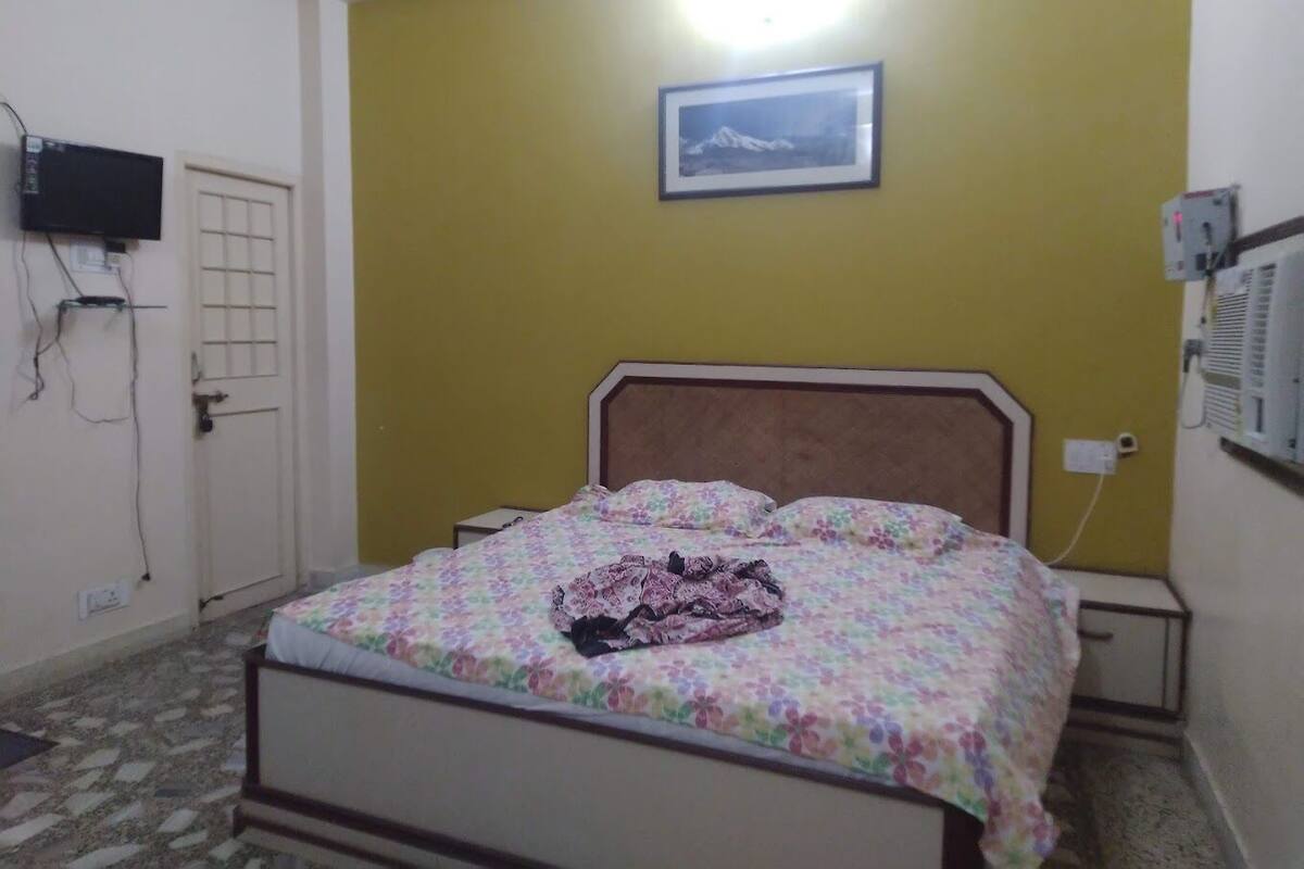 Un dormitorio con una cama, una mesita de noche, un televisor de pared y un cuadro enmarcado.