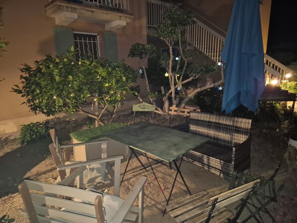 An outdoor patio area with a table and chairs, a small tree, and a staircase leading to a balcony.