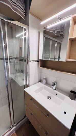 Ein modernes Badezimmer mit einer Duschkabine aus Glas, einem weißen Waschbecken und einem Holz-Waschtisch.