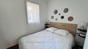 Une chambre avec un grand lit, une fenêtre avec des rideaux, une table de chevet avec une lampe et des éléments de décoration murale.