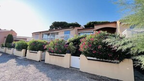 Une rangée de maisons avec une allée en gravier, un portail blanc et des arbustes en fleurs.