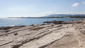 Una costa rocosa amb una vista clara del mar i muntanyes allunyades.