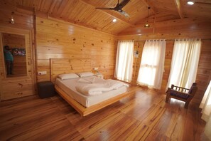 A wooden cabin bedroom with a bed, a bench, and a ceiling fan. - The Candlewood Resort (Murud)