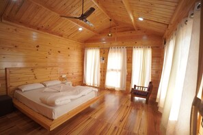 A wooden cabin bedroom with a bed, a chair, a ceiling fan, and curtains. - The Candlewood Resort (Murud)