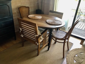 A dining table with woven placemats, wooden chairs with white cushions, and a dark wooden cabinet.
