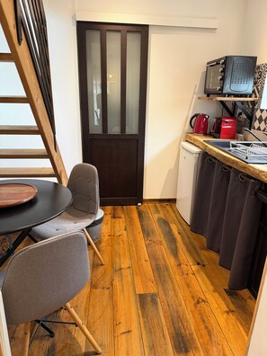 Une cuisine compacte avec un plancher en bois, une table à manger avec des chaises, un four à micro-ondes, une bouilloire et un petit réfrigérateur.