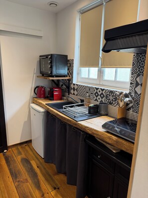 Une cuisine compacte équipée d’un four à micro-ondes, d’une bouilloire et d’un grille-pain, le tout posé sur un plan de travail en bois.