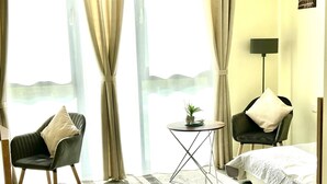 A hotel room with a bed, two chairs, a small table, and a view of the sea. - LikeDaheim Apartments (Rosbach vor der Hoehe)