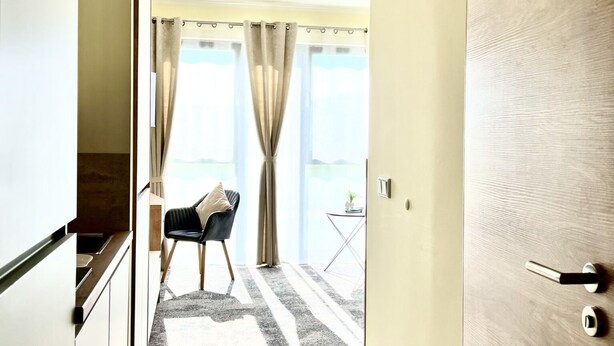 A hotel corridor with a view to a balcony, a chair, and a small table. - LikeDaheim Apartments (Rosbach vor der Hoehe)
