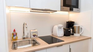 Moderni keittiö, jossa on ruostumattomasta teräksestä valmistettu allas, Bosch-mikroaaltouuni, kahvinkeitin ja Tassimo-kahvikapselikone.