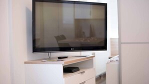 Seinälle asennettu litteänäyttöinen televisio, joka on sijoitettu puisen TV-tason päälle. Mukana kaukosäädin ja kaapelivastaanotin.