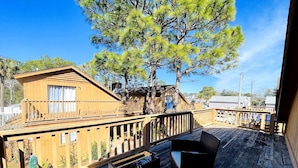 A wooden deck with outdoor furniture, a wooden building with a balcony, and trees in the background.