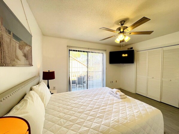 A bedroom with a bed, a ceiling fan, a TV, and a sliding door to a balcony.