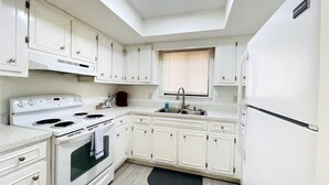A compact kitchen with white cabinetry, a built-in oven, a sink, and a refrigerator.