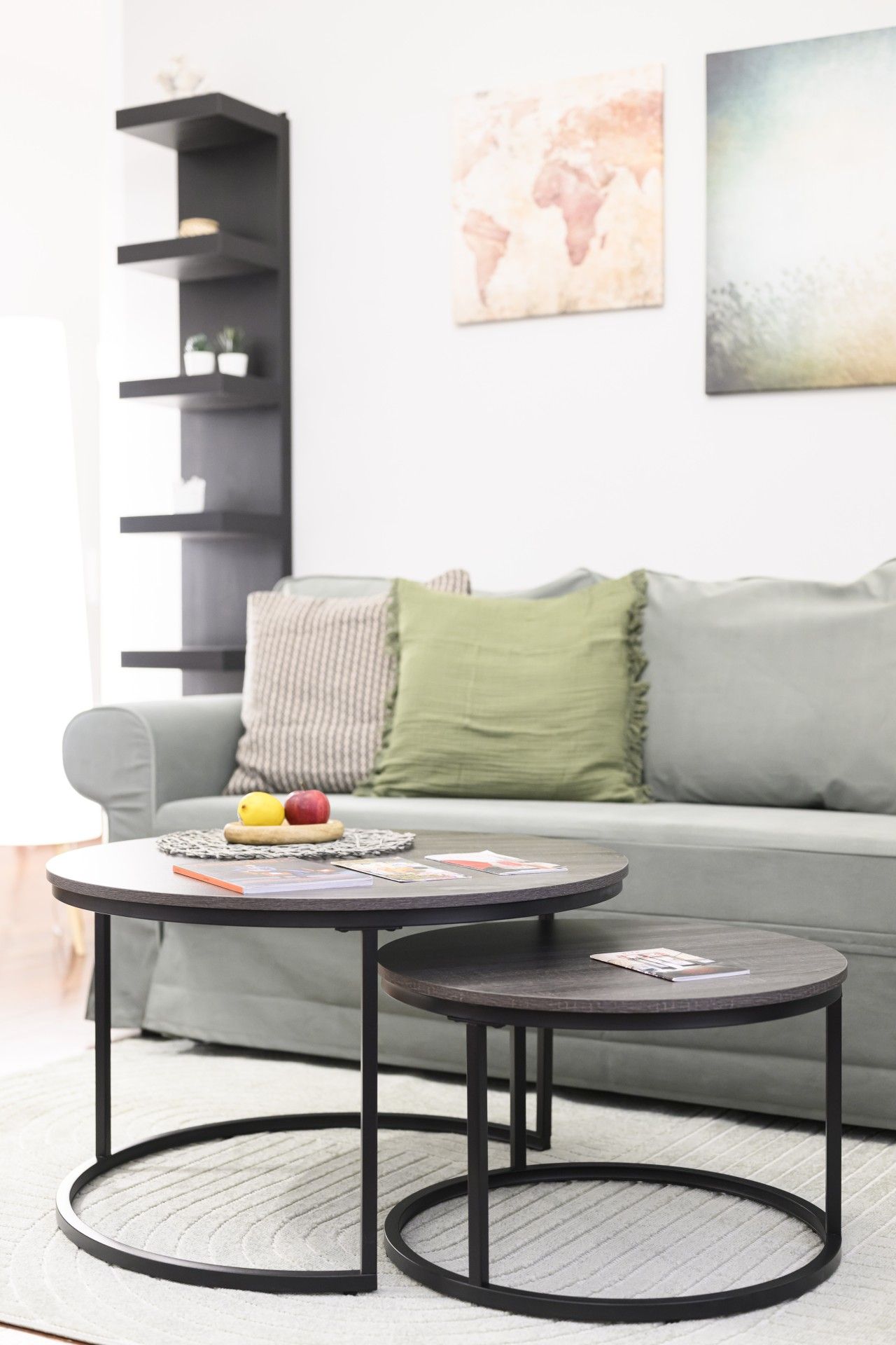 Ein modernes Wohnzimmer mit einem grauen Sofa, einem runden Couchtisch mit Zeitschriften und einem kleinen Beistelltisch.