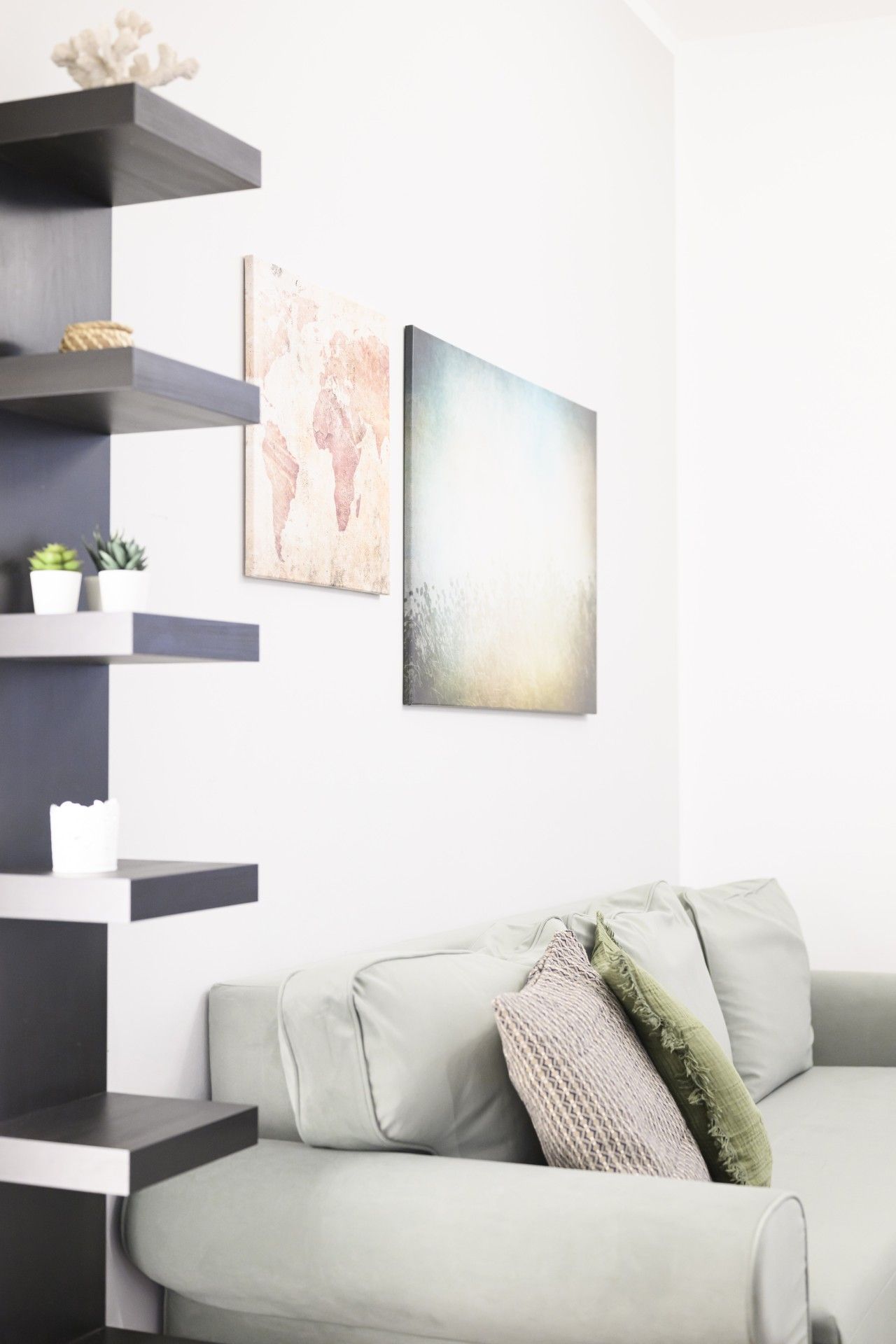 A modern living room with a grey sofa, a black shelving unit, and two abstract paintings.