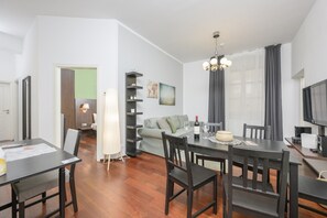 A modern living room with a dining area, a sofa, a TV, and a large window with curtains.