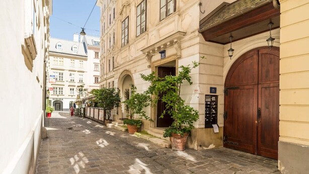 Eine enge Kopfsteinpflasterstraße mit historischen Gebäuden, großen Holztüren und Topfpflanzen.