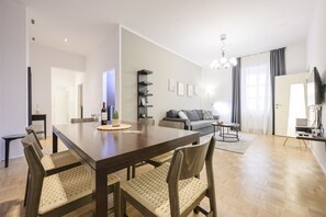 Una sala de estar moderna con comedor, un sofá gris, un televisor y una araña.