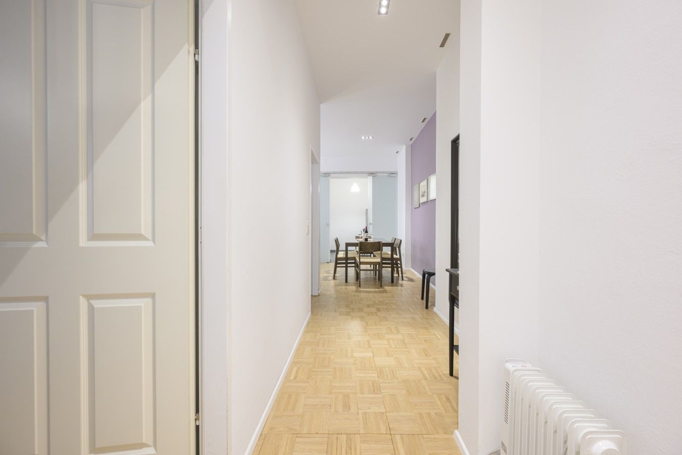 A hallway with a dining area at the end, featuring a table and chairs.