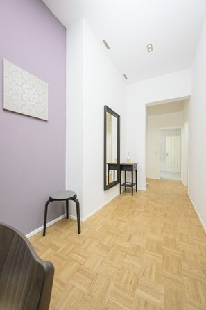 Una habitación con suelo de espiga, un espejo, una pequeña mesa y una silla.