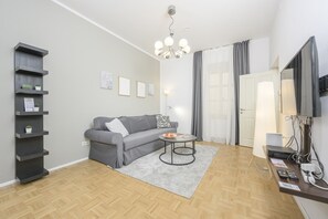 A modern living room with a grey sofa, a coffee table, a bookshelf, a flat-screen TV, and a chandelier. - Premium Business Apartment (Vienna)