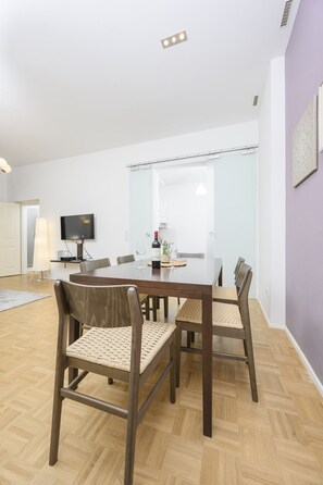 Uma zona de refeições com mesa e cadeiras de madeira, televisão fixada na parede e decoração moderna.