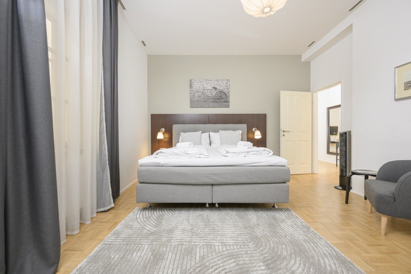 Ein modernes Schlafzimmer mit Bett, Nachttischlampen, einem Kopfteil, einem Teppich und einem Sessel.
