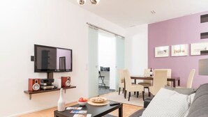 Ein modernes Wohnzimmer mit Flachbildfernseher, einem Couchtisch mit Zeitschriften, einer Couch und einem Essbereich mit Stühlen und einem Tisch.