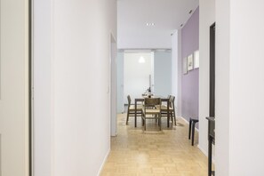 Un pasillo que conduce a un comedor con una mesa lista para dos personas, suelo de madera y una puerta a la derecha.