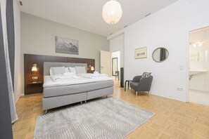 Un dormitorio moderno con una cama doble, lámparas de noche, un sillón gris y un espejo grande.