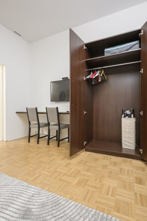 Una habitación con un armario de madera, una mesa de comedor con sillas y un televisor en la pared.