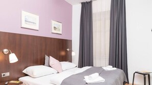 Ein Hotelzimmer mit einem Bett, zwei Nachttischlampen, einem Nachttisch, einem Fenster mit Vorhängen und zwei gerahmten Bildern an der Wand.