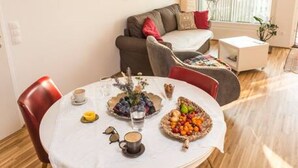 Un comedor con una mesa redonda dispuesta para dos personas, un sofá y un balcón con barandilla.