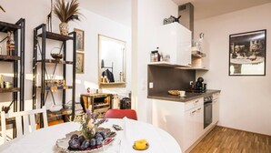 Una cocina moderna con armarios blancos, encimera negra y horno empotrado. Hay una zona de comedor con una mesa redonda y sillas, además de una pequeña silla roja.