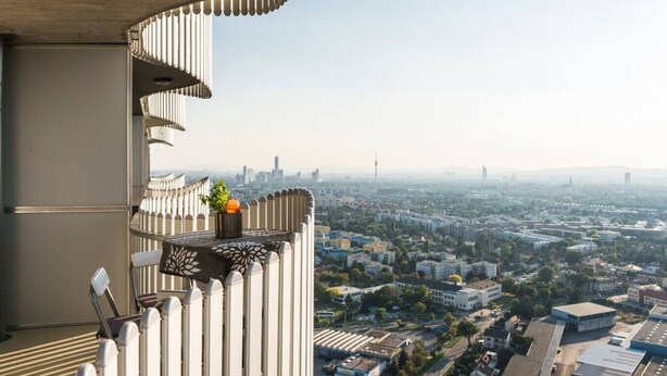 Un edificio alto con un balcón que tiene barandilla decorativa y una planta en maceta.