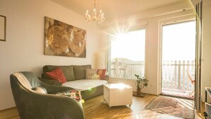 Una sala de estar con sofá, sillón, mesa de centro, candelabro, un cuadro grande y un balcón con vistas.