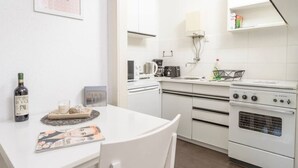 A modern kitchen with white cabinets, a white countertop, a stove, a sink, and a coffee maker. There is a framed picture on the wall and a bottle of wine on the counter. - Kriehubergasse / Margaretengürtel (Vienna)