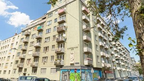 A multi-story building with balconies, a mural on the ground floor, and several parked cars. - Kriehubergasse / Margaretengürtel (Vienna)