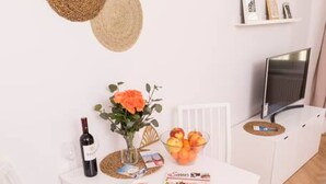 A dining area with a white table, chairs, a vase with flowers, a bowl of fruit, a wine bottle, and a magazine. - Heart of Ottakring in Vienna (Vienna)