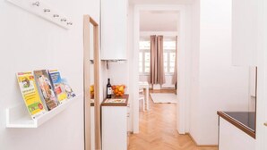 A bright hallway with a white shelf holding books, a wooden door, and a view into a dining area with a table and chairs. - Heart of Ottakring in Vienna (Vienna)