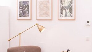 A room with a brown armchair, a small white side table with a plate of cookies, and three framed abstract artworks on the wall. - Heart of Ottakring in Vienna (Vienna)