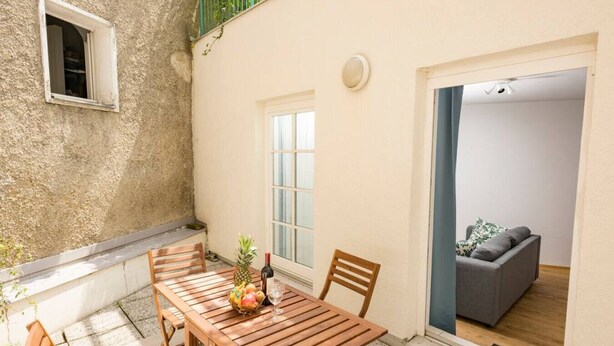 A patio with a wooden table and chairs, a small window, and a view into a room with a sofa.