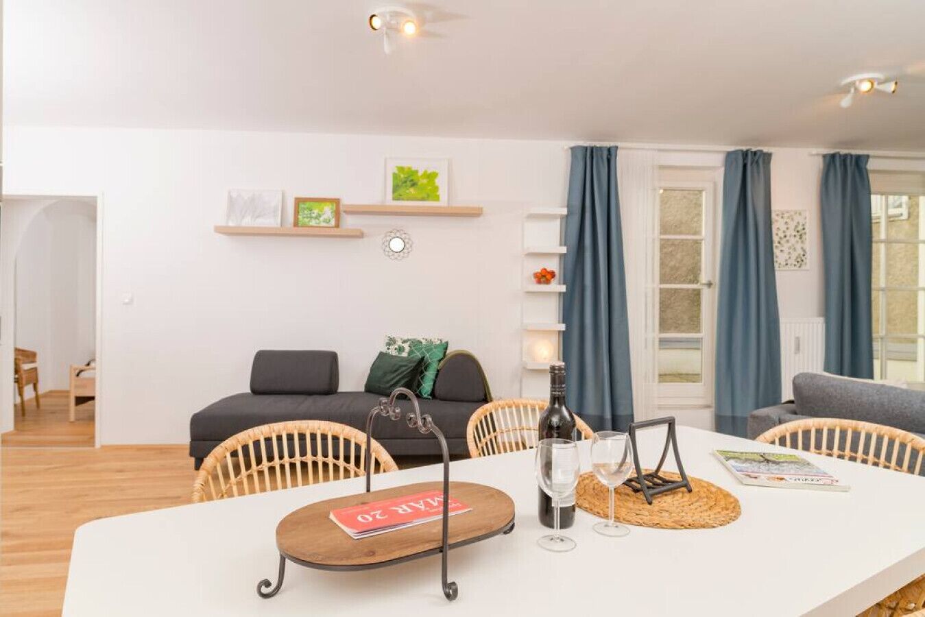 A modern living room with a white sofa, a dining table with chairs, and a kitchen area in the background.